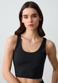 Czarny crop top wykonany z gładkiego materiału, z szerokim dekoltem i bez zapięć, oferujący dopasowaną sylwetkę.