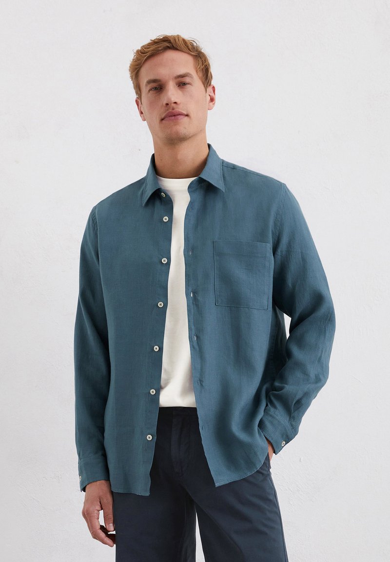 Teal knoopshirt van lichtgewicht stof met een borstzak, gecombineerd met een witte ronde hals t-shirt, heeft een relaxte pasvorm en een gladde textuur.