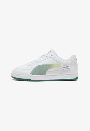 Baskets basses blanches Puma avec une bande dégradée verte, une semelle verte et une étiquette avec le logo de l’équipe de Formule 1 sur le côté.