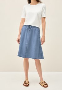 Lys blå denimnederdel med elastisk talje og snøredetalje, parret med en ensfarvet hvid t-shirt med korte ærmer og brune sandaler.
