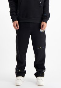Zwarte sweatpants met een relaxed fit, voorzien van verfspetters in blauw en geel, en een logo op de linker dij. Gemaakt van een katoenen mix.
