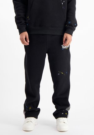 Schwarze Sweatpants mit einer lockeren Passform, versehen mit Farbspritzern in Blau und Gelb sowie einem Logo auf dem linken Oberschenkel. Hergestellt aus einem Baumwollmix.