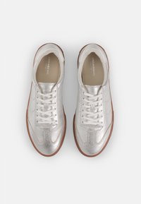 Silver metallic sneakers with a textured finish, white laces, and a light brown rubber sole. Minimalist design with subtle branding.