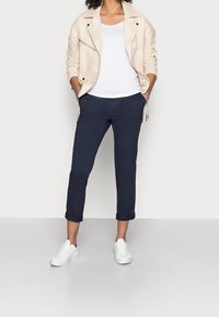 Béžová kožená motocyklová bunda, bílý tričko, námořnické zkrácené kalhoty a bílé tenisky. Bunda má zipy a srolované manžety na kalhotách.