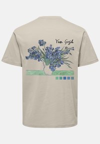 T-shirt in cotone beige con stampa di un fiore di iris blu e dettagli verdi sul retro, con la scritta "Van Gogh" in un font elegante.