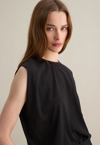 Top nero senza maniche con scollo rotondo, realizzato in tessuto liscio, cade dolcemente sul corpo, caratterizzato da un design minimalista e senza accenti visibili.