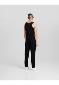 Top negro sin mangas y vaqueros negros usados por una persona, presenta un diseño simple y una forma ajustada, combinados con zapatillas blancas.