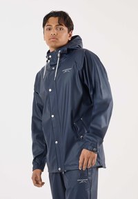 Marineblauw waterdicht jack met capuchon, drukknoopsluiting, elastische manchetten en voorzakken. Heeft een logo op de borst en een gladde, glanzende textuur.