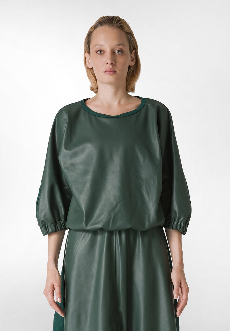 Top de símil cuero verde con escote redondo, mangas abullonadas y puños elásticos. Textura suave con un ajuste relajado, combinado con una parte inferior a juego.