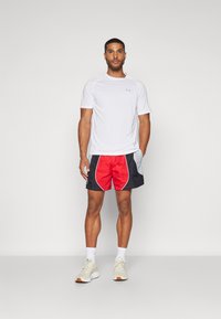 Hvit kortermet skjorte, røde og svarte treningsshorts med buede sidelommer, og lette joggesko med hvite og beige detaljer.