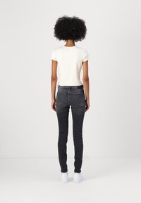 Camiseta blanca de manga corta combinada con jeans ajustados gris oscuro y zapatillas blancas, vista desde la parte posterior sobre un fondo simple.