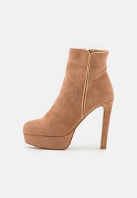 Bottine en daim marron clair avec un talon stiletto haut, un plateau à l'avant et une fermeture éclair à l'arrière. Texture lisse et silhouette élancée.