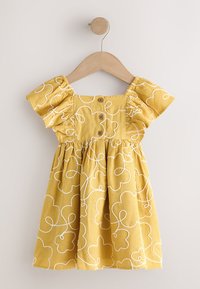 Robe jaune pour tout-petit avec manches bouffantes, boutons en bois et broderie florale blanche abstraite suspendue sur un cintre en bois.