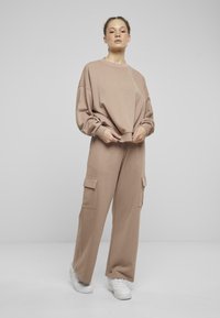 Completo da loungewear a due pezzi in morbido beige. Include una felpa a girocollo e pantaloni a gamba larga con tasche cargo laterali. Sneakers bianche.