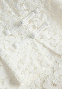 Gros plan sur un tissu en dentelle florale blanche avec deux boutons décoratifs blancs en forme de nœuds sur des boucles de tissu.