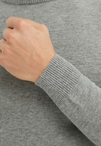 Pull gris en tissu doux, avec des poignets côtelés. Texture lisse avec un col tricoté et une coupe ajustée.