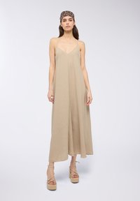 Abito maxi beige con spalline sottili e scollo a V. Realizzato in tessuto testurizzato, presenta una silhouette fluida. Abbinato a sandali con plateau in espadrilles.