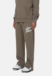 Szary, oversize'owy hoodie z przednią kieszenią, w połączeniu z dopasowanymi spodniami dresowymi z napisem "Good for Nothing" na lewym udzie. Białe sneakersy.