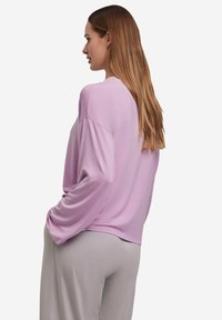 Hellviolettes Langarmoberteil mit entspannter Passform, rundem Ausschnitt und herabgesetzten Schulternähten. Kombiniert mit grauen Hosen für einen lässigen Look.