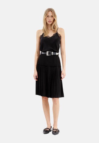 Vestito nero con top in satin e bordi in pizzo, vita con cintura e gonna plissettata. Abbinato a scarpe nere flat.