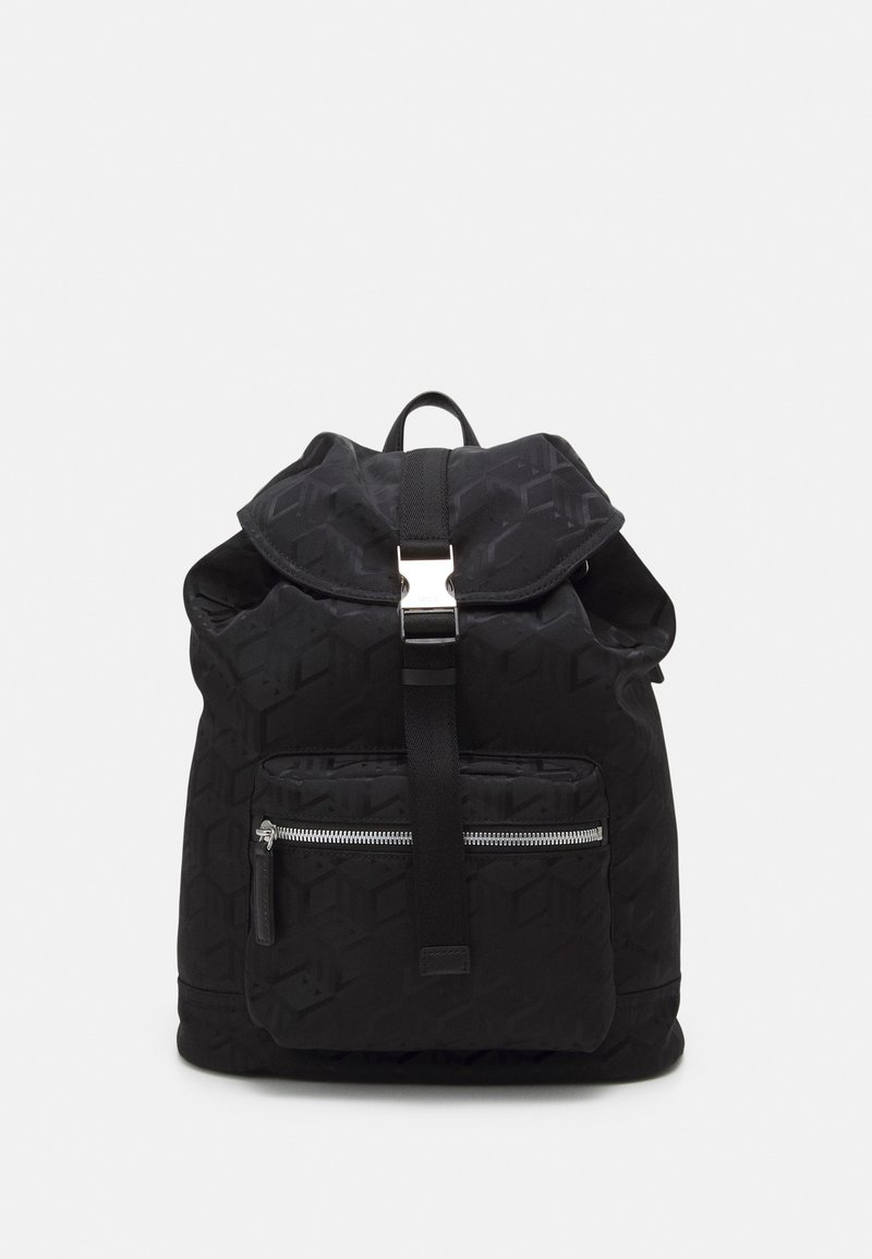 Sac à dos noir texturé avec poche frontale zippée et rabat supérieur maintenu par une boucle et une sangle en métal, sur un fond clair uni.