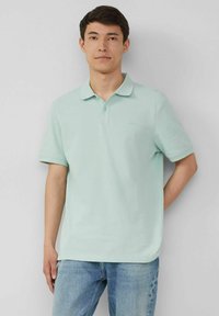 Minzgrünes Polohemd aus weichem Baumwollstoff, mit klassischem Kragen und zwei Knöpfen, kombiniert mit hellblauen Jeans.