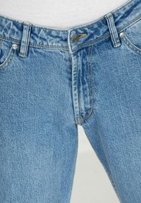 Jeans de mezclilla azul claro con cierre de botón, costuras visibles y un acabado texturizado. Cuenta con bolsillos estándar y pasadores para cinturón.