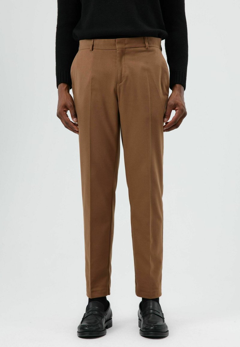 Bruine op maat gemaakte broek met een gladde textuur, voorzien van een recht pijpontwerp en zijzakken. Draagt bij zwarte loafers.