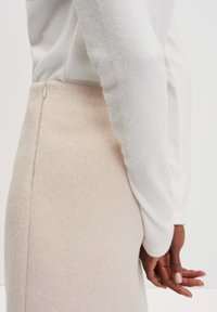 Helle beige Rock mit einer weichen, strukturierten Oberfläche, der an der Seite einen verdeckten Reißverschluss hat. Kombiniert mit einem weißen Langarmshirt.