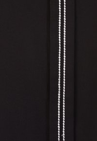 Tissu noir présentant deux lignes parallèles de petits clous en argent, créant un effet texturé et décoratif à la surface.