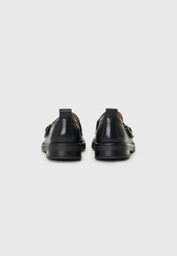 Scarpe in pelle nera con tacco basso, caratterizzate da una superficie liscia, un design minimalista e un accento di fibbia dorata sul lato.
