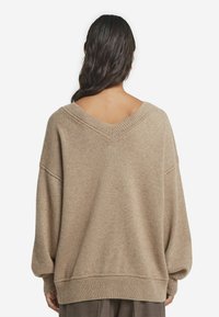 Sweter w serek w jasnobrązowym kolorze, luźny krój, obniżone ramiona, ściągacze przy mankietach i hemie, teksturowany materiał dzianinowy, minimalne detale.