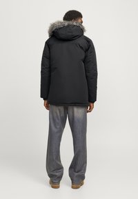 Parka noire avec capuche doublée de fourrure, dotée d'un extérieur résistant, d'une coupe décontractée et de poignets côtelés, associée à un pantalon en denim bleu clair.