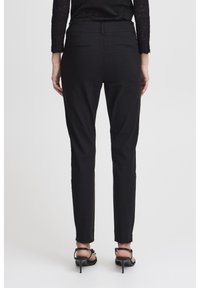 Black tailored trousers with a slim fit, featuring back pockets and a smooth texture, paired with black high-heeled sandals.