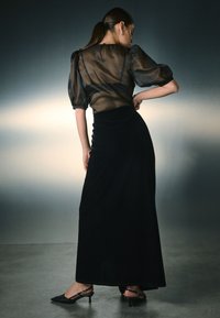 Black, sheer blouse with puff sleeves and button closure at the back, paired with a black velvet maxi skirt and pointed-toe heels.