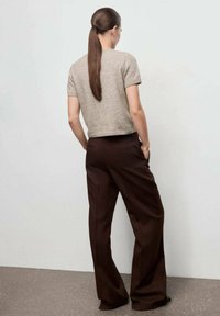Top corto a maniche corte di colore grigio chiaro a maglia abbinato a pantaloni palazzo di colore marrone scuro. Il top ha una vita aderente, mentre i pantaloni presentano tasche laterali.