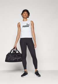 Hvit ermeløs tank topp med svart "PUMA"-logo, svarte leggings, svarte joggesko og en svart duffelbagen med hvite detaljer.