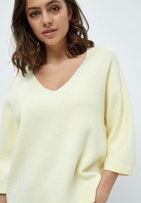 Maglione a V con vestibilità ampia in morbido tessuto giallo chiaro. Presenta maniche a tre quarti e una finitura liscia e lavorata.