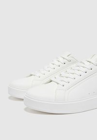 Białe sneakersy mają gładką skórzaną cholewkę, okrągły czubek, sznurowany fason oraz teksturowaną gumową podeszwę dla lepszej przyczepności. Minimalistyczny styl bez wzorów.
