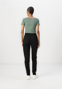 Grön figurnära t-shirt med rund halsringning och korta ärmar, tillsammans med svarta byxor med elastisk midja och sidofickor.