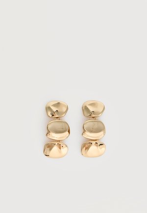 Boucles d’oreilles pendantes ton or avec trois segments irréguliers, lisses et arrondis empilés verticalement sur un fond clair uni.