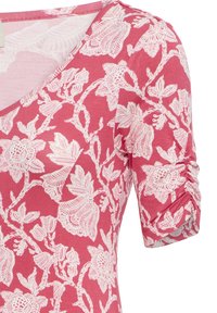 Vêtement rose avec motif floral blanc et manches 3/4 froncées, doté d'un décolleté en V et d'un tissu léger.