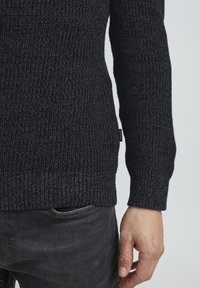 Maglione grigio scuro a maglia, con texture a coste, scollo rotondo, maniche lunghe, piccolo etichetta sul lato, abbinato a jeans scuri.