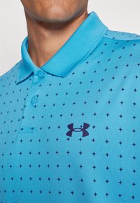 Polo de culoare albastră deschisă, cu un material texturat, având un model cu mici stele navy și un logo Under Armour navy pe piept.