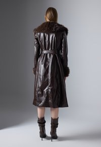 Cappotto lungo in pelle marrone scuro con motivo a coccodrillo, colletto e polsini in pelliccia. Chiuso con una cintura, finisce sotto il ginocchio. Design elegante.