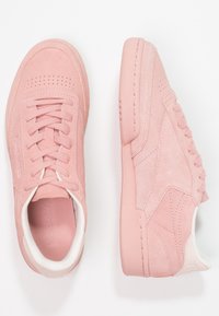 Paire de baskets en daim rose avec lacets, une chaussure montrant la vue de dessus et l'autre la vue latérale sur fond blanc.