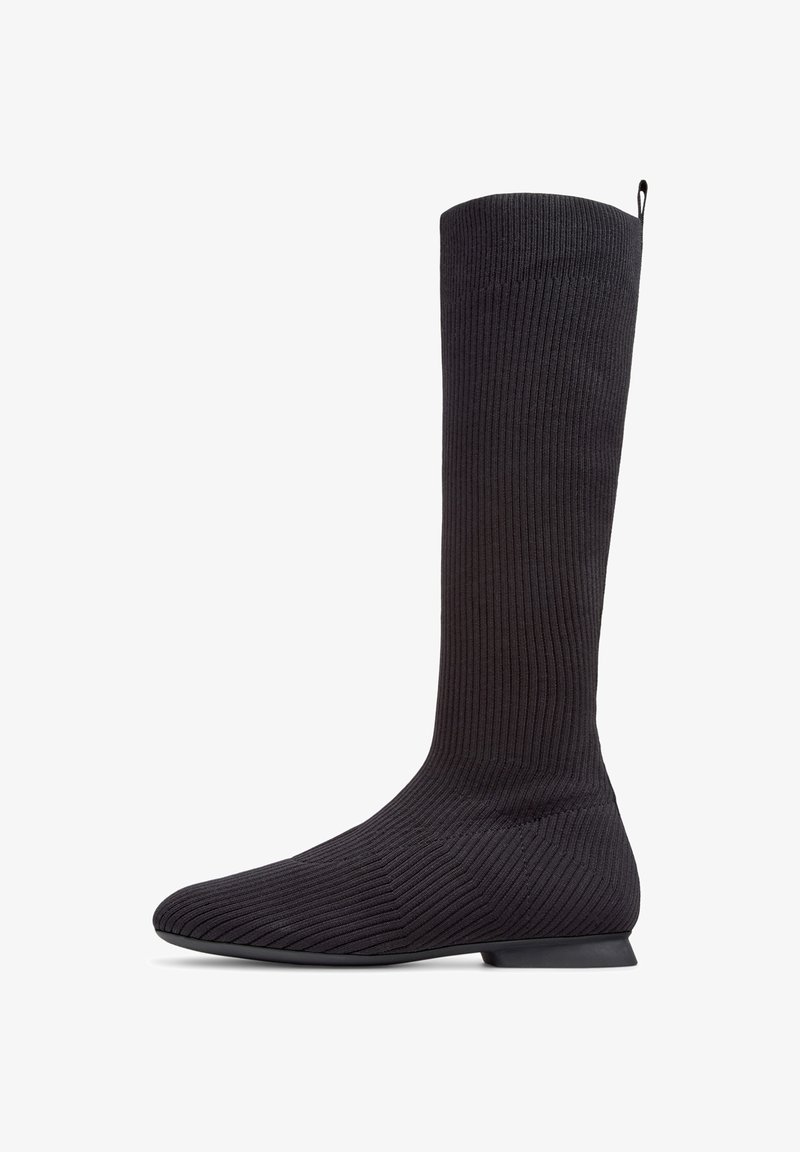 Bota negra de punto hasta la rodilla con textura acanalada, puntera afilada y pequeño tacón plano, que cuenta con una pestaña en la parte superior.