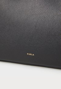 Melnas ādas soma ar graudainu tekstūru, kurai ir zeltīts "FURLA" logotips. Vienkāršs, taisnstūrveida dizains ar tīrām līnijām un bez papildu aprīkojuma.