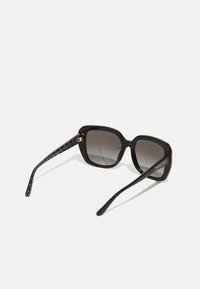 Gafas de sol con un grueso marco de plástico negro, lentes oscuros en degradé y una patilla negra decorada con un patrón que presenta acentos de hardware dorado.