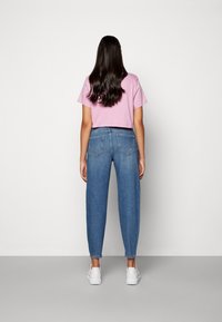 Růžové zkrácené tričko spárované se světle modrými volnými džíny a bílými teniskami. Hladká látka a klasický design s pěti kapsami.